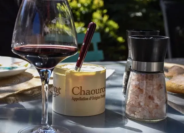 Glass of red wine, Chaource cheese with a knife, and salt and pepper grinders on an outdoor table.