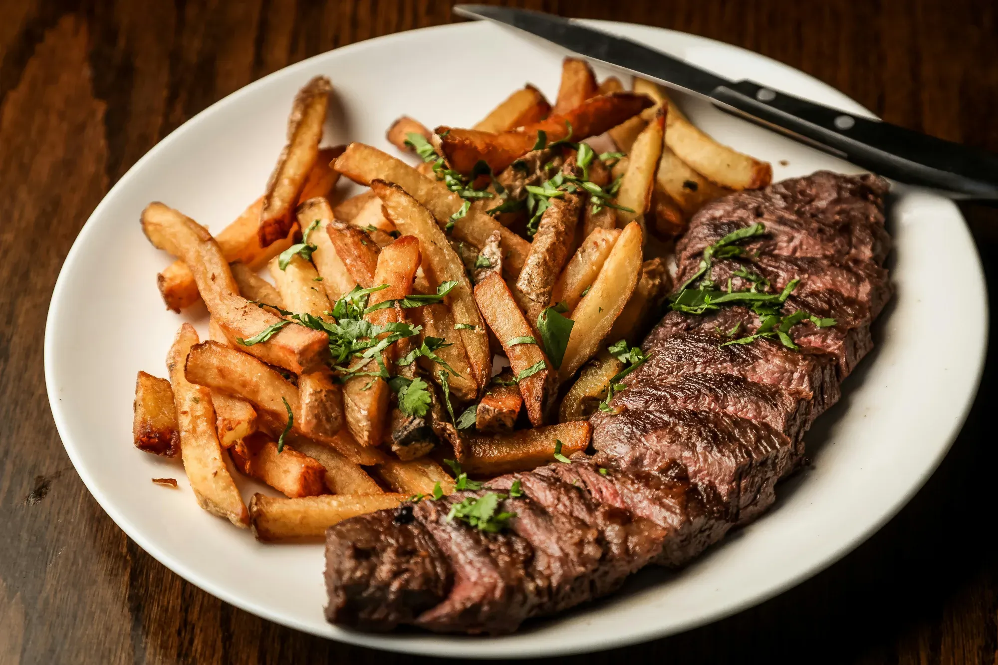 Un plato de steak frites, con un filete a la parrilla en rodajas junto a un montón de patatas fritas con hierbas frescas.
