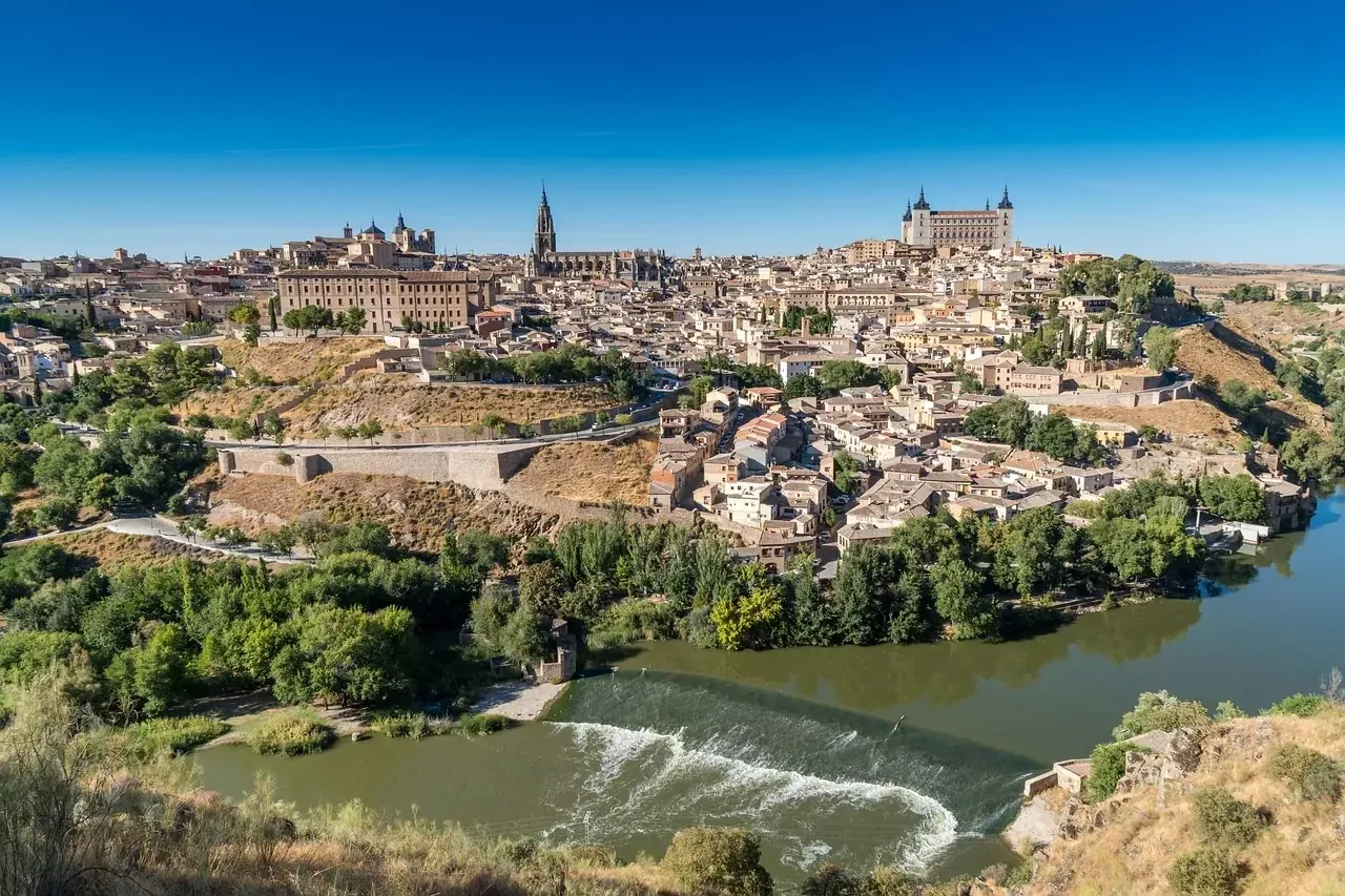 Panoramablick auf die historische Stadt Toledo, Spanien, an einem sonnigen Tag mit dem Tejo im Vordergrund.