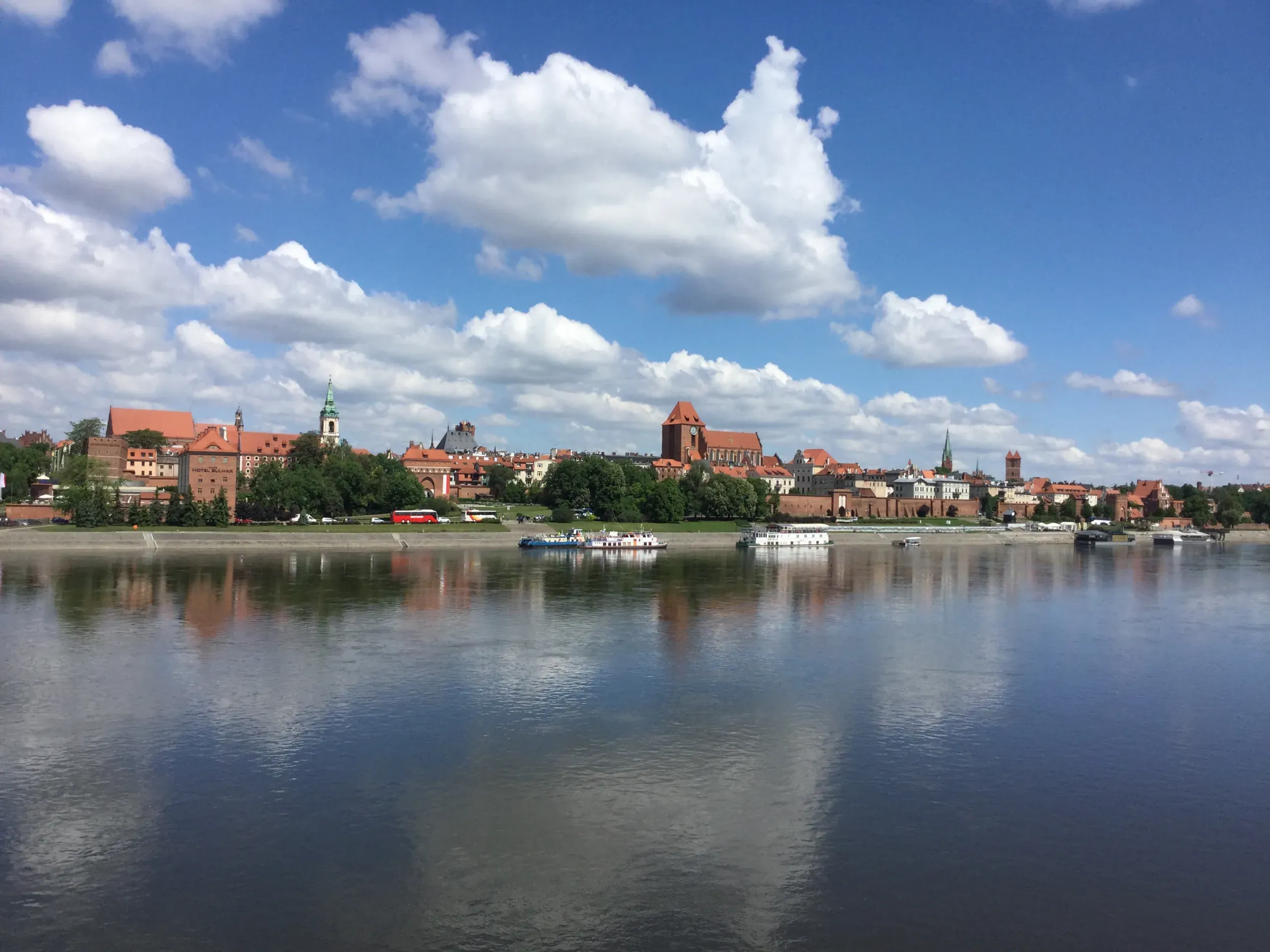 Panoramic view of Toruń Old Town skyline along the Vistula River, with historic buildings and red roofs.