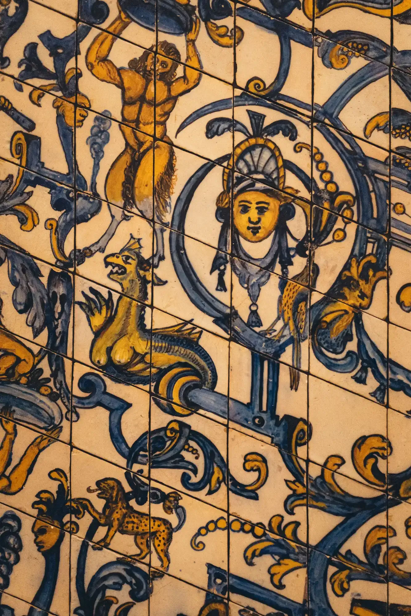 Zbliżenie na żółto-niebieskie płytki ceramiczne z postaciami mitologicznymi, w tym satyrem, smokiem i lampartem.