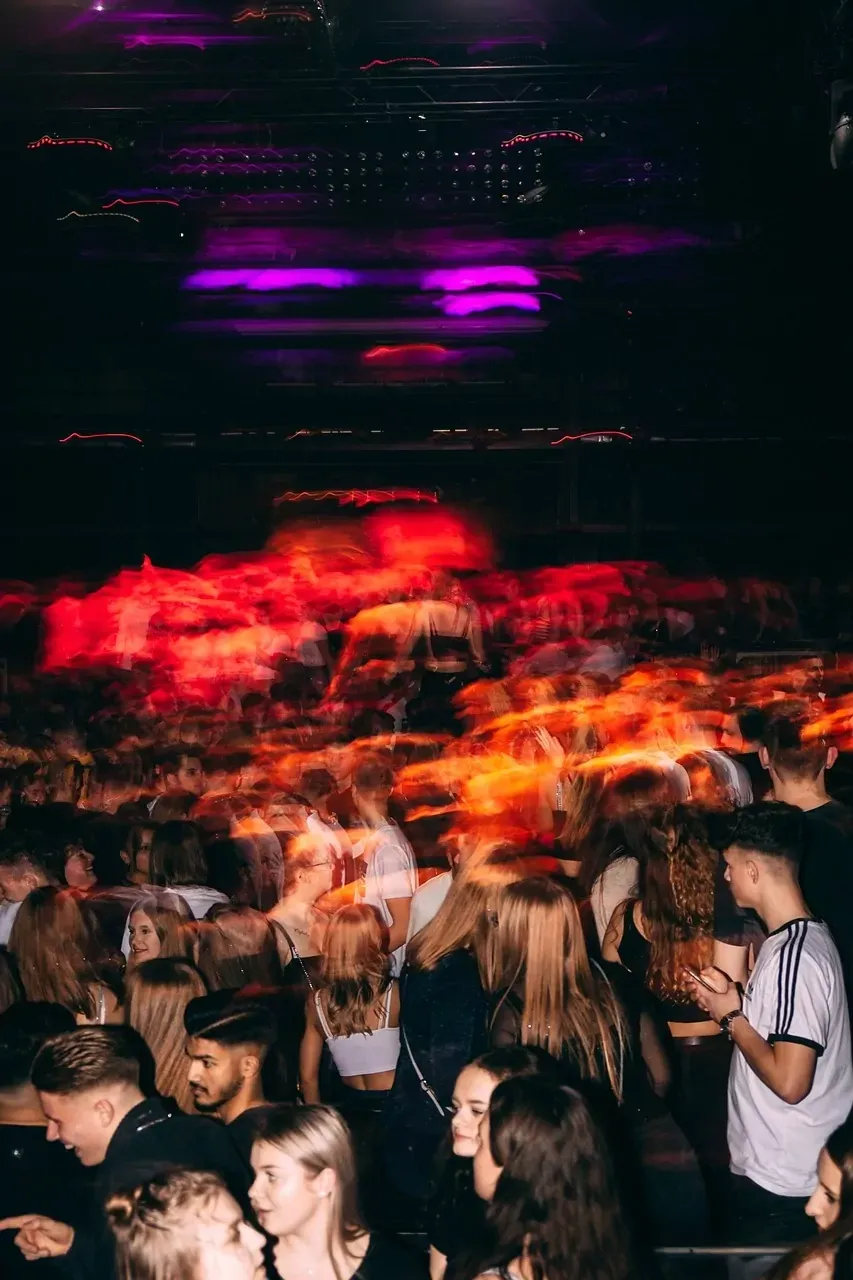 Verschwommene Menschen in einem dunklen Nachtclub, beleuchtet von leuchtend roten und violetten Lichtern, die sich in der Men