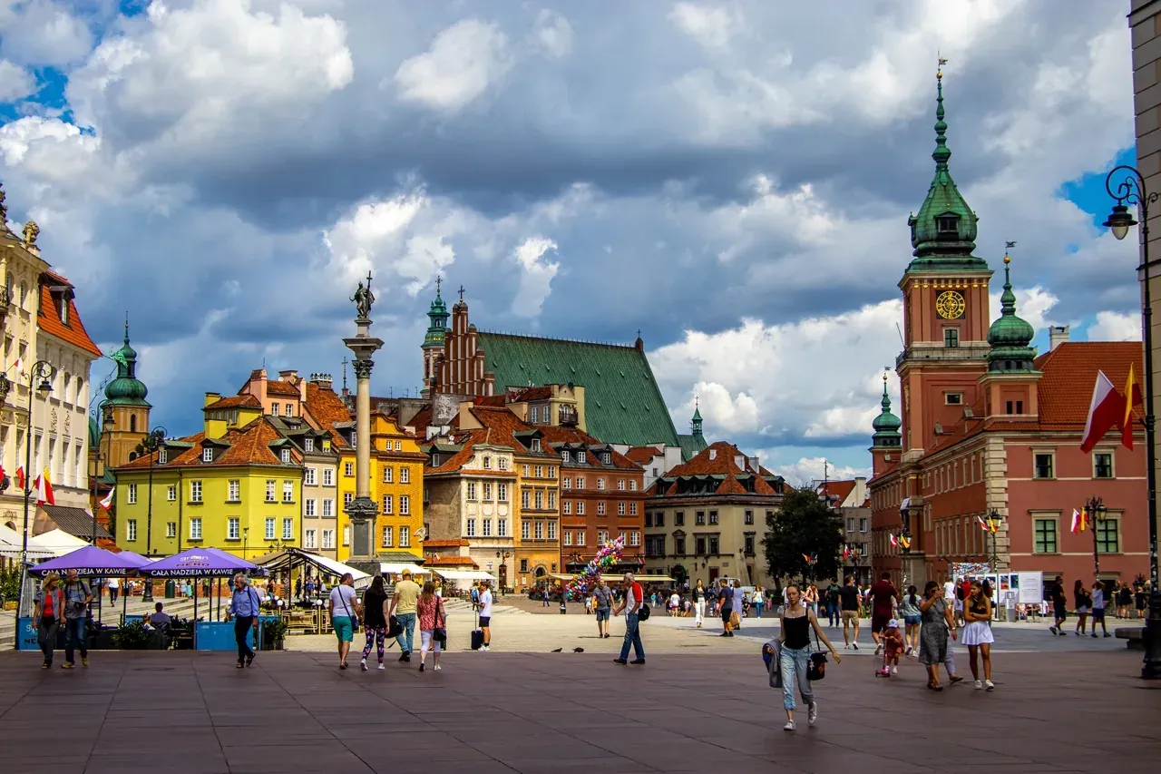 Castle Square in Warsaw with Sigismund's Column, colorful tenement houses, and the Royal Castle under a cloudy sky.