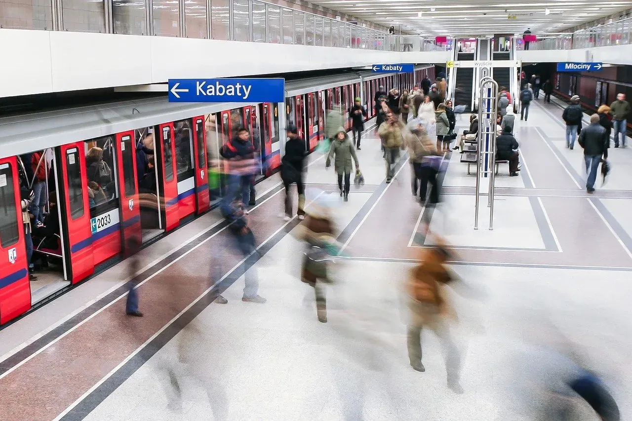 Long exposure shot of people moving on a clean, modern metro platform with a red train and 'Kabaty' sign.