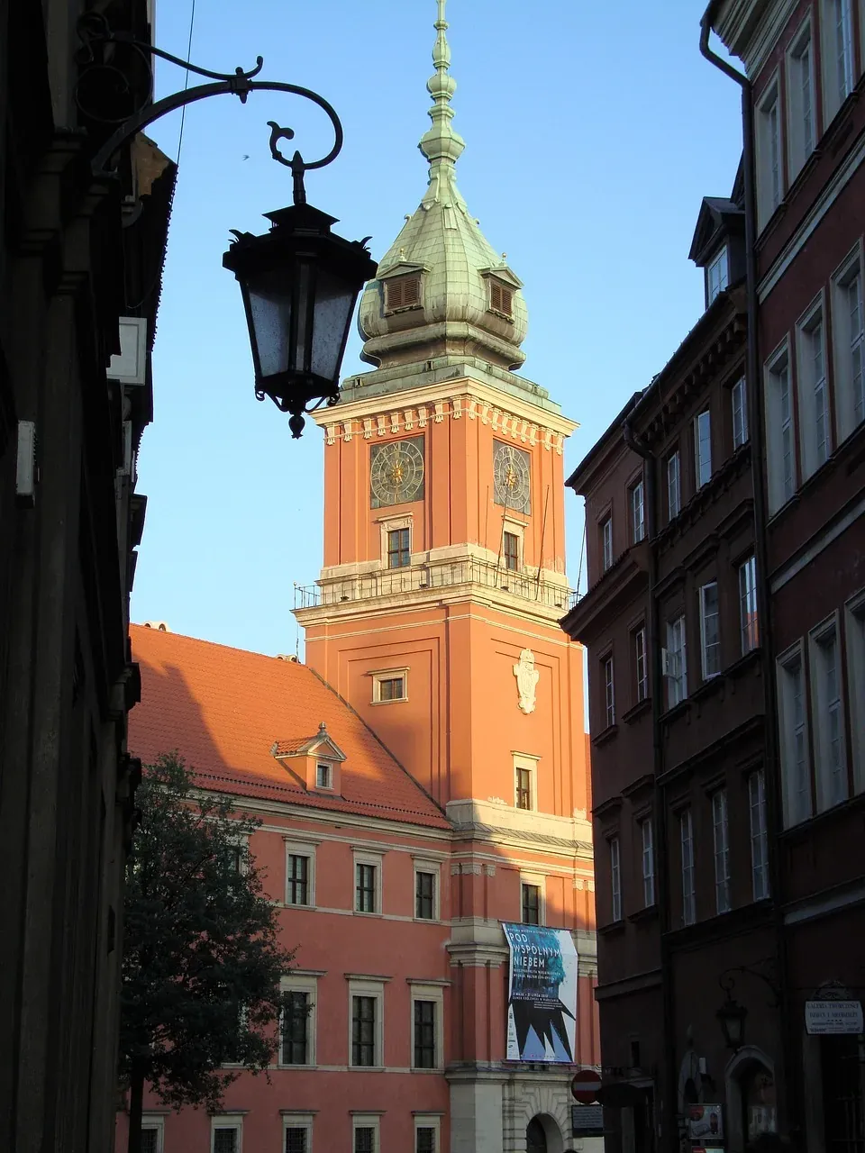 Ein pfirsichfarbener Uhrturm mit grüner Kuppel und zwei Zifferblättern, eingerahmt von historischen Gebäuden und einer schwar