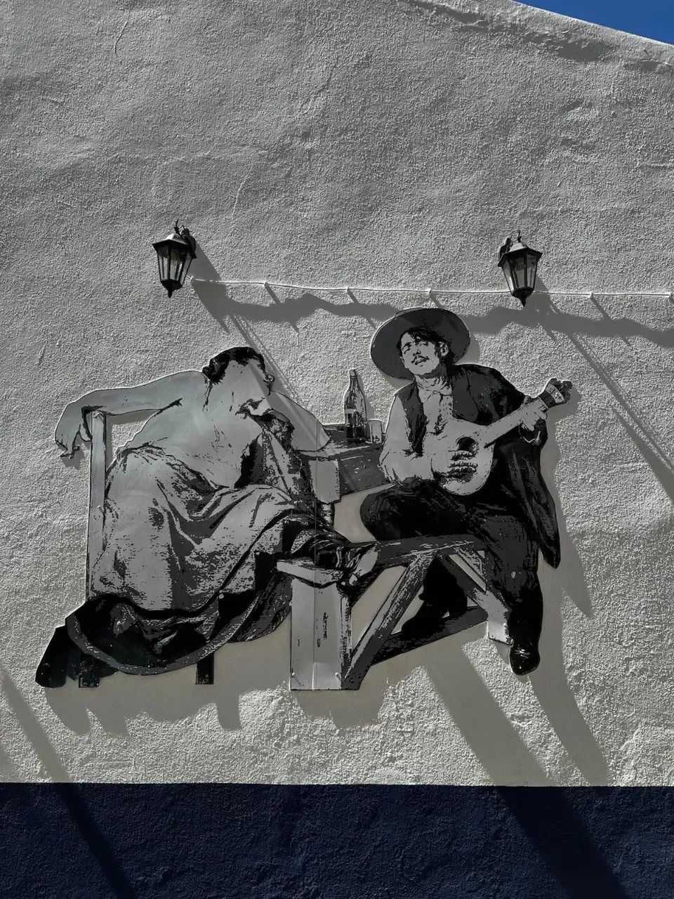 Wall cutout art depicting a fado guitarist and a listening woman on a white textured wall.