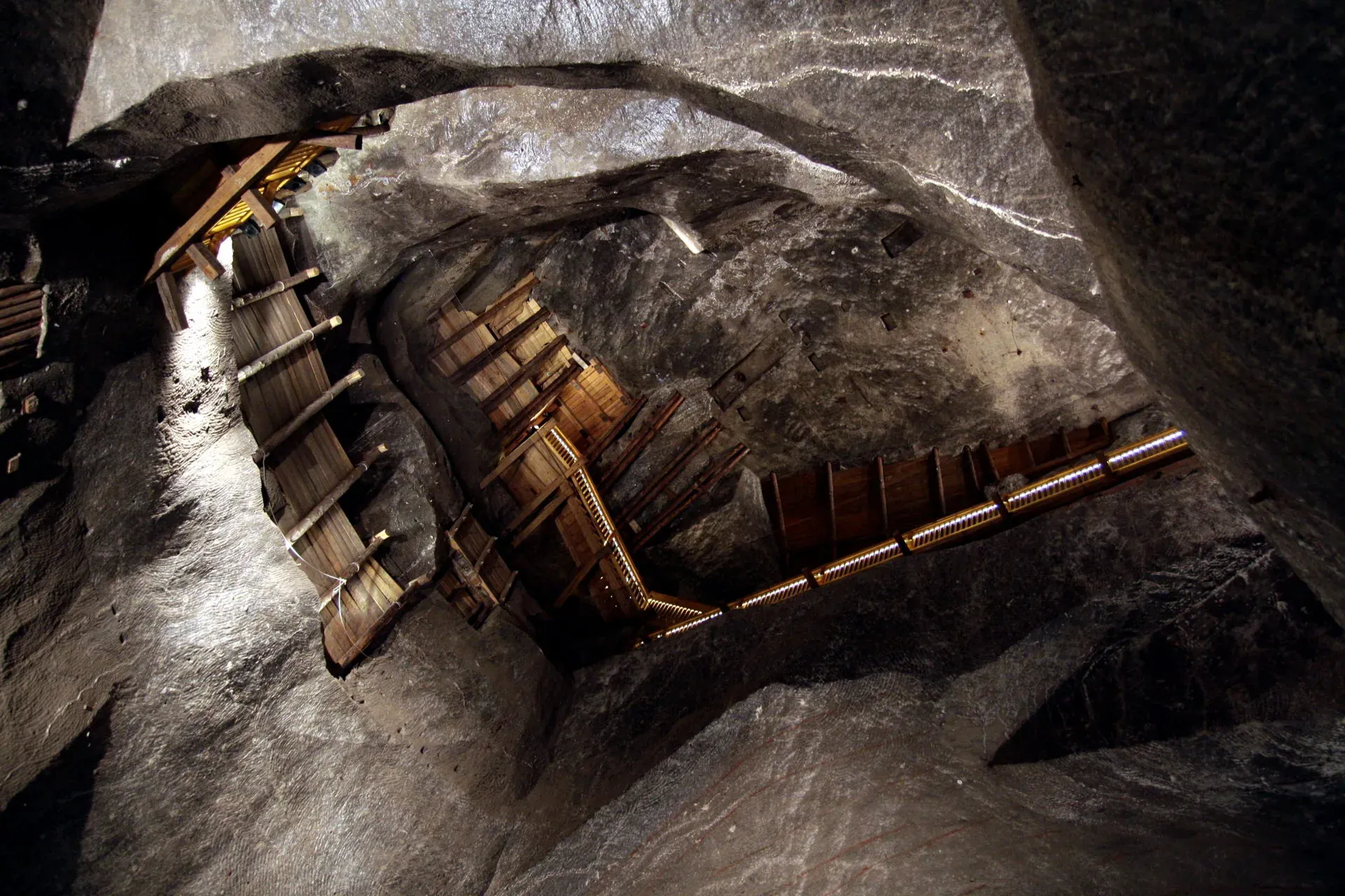 View upwards in the Wieliczka Salt Mine, showing rough-hewn salt walls and illuminated wooden support structures.