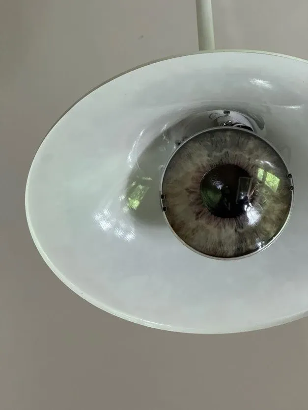 Close-up of a white ceiling lamp where the lightbulb is designed to look like a realistic human eye.