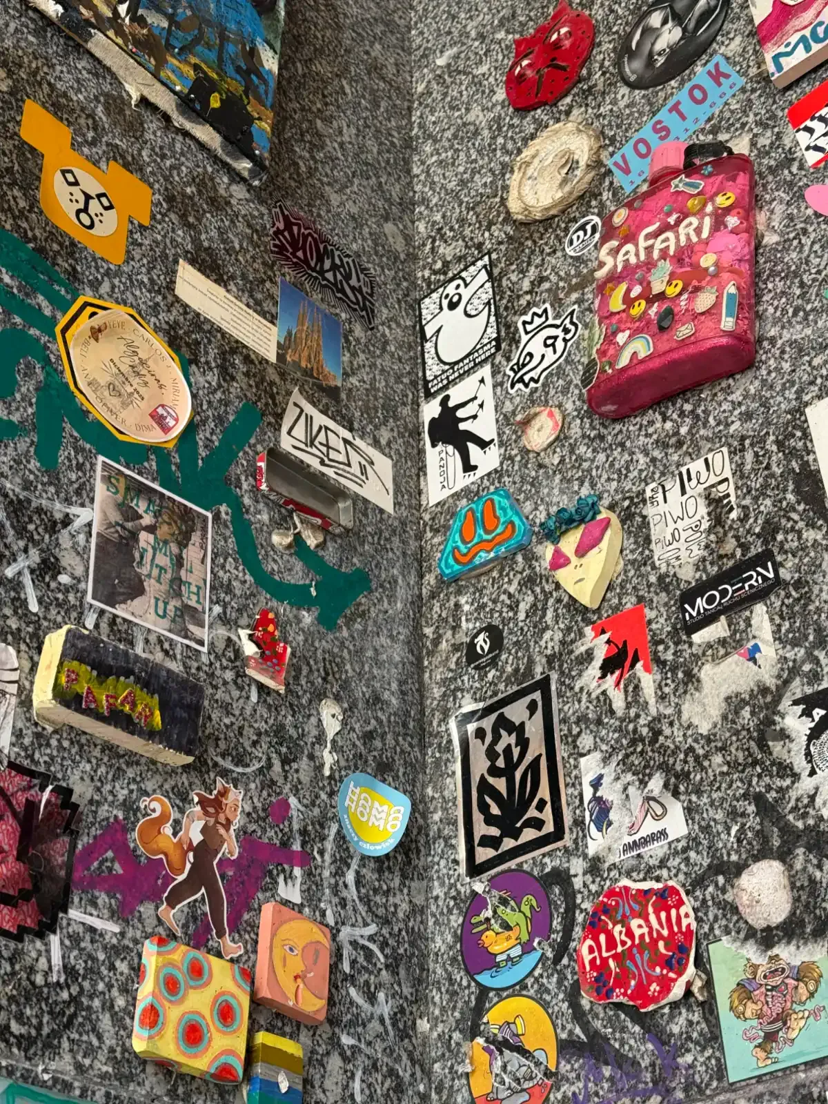 A corner of a granite wall covered in a dense collage of colorful stickers, small objects, and graffiti tags.
