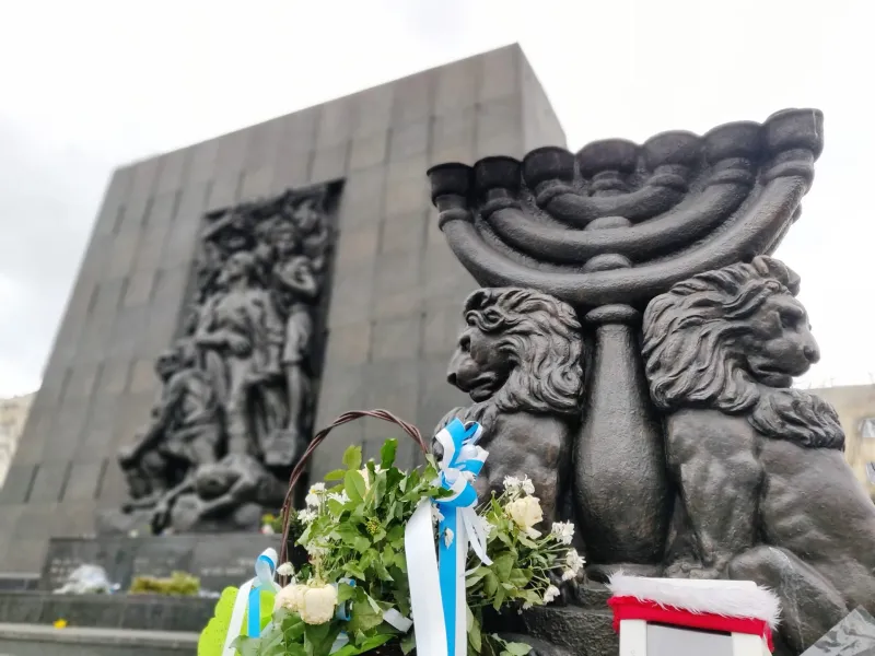 Pomnik Bohaterów Getta w Warszawie z menorą i kwiatami.