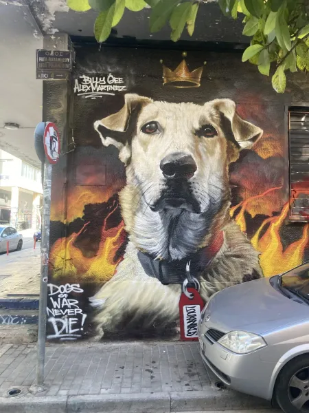 Large street art mural of a light-furred dog with a golden crown and flames in the background, on an Athens street.