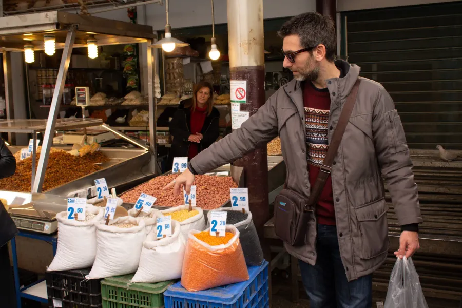 Un guía turístico muestra a los turistas varias legumbres y frutos secos en un vibrante mercado de Atenas, Grecia.
