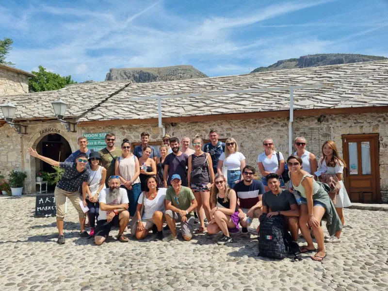 Happy tourists on a group tour in Berat, Albania, posing in front of a historic stone building.
