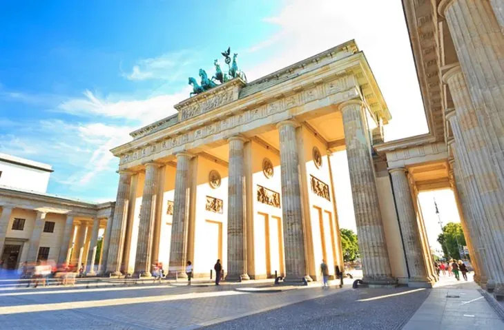 La Puerta de Brandeburgo en Berlín en un día soleado, con sus grandes columnas proyectando largas sombras sobre la plaza.