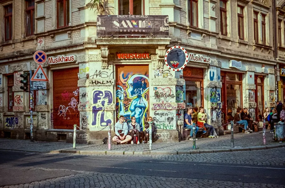 A vibrant street scene in Dresden Neustadt, showcasing graffiti art and a group of people enjoying the atmosphere.