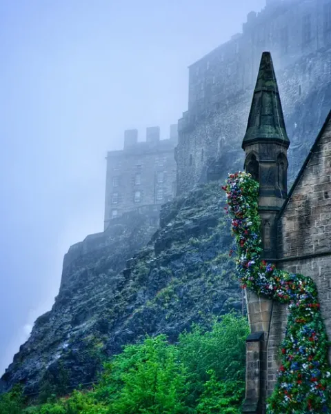 Castillo de Edimburgo envuelto en niebla, con un edificio decorado con flores en primer plano.