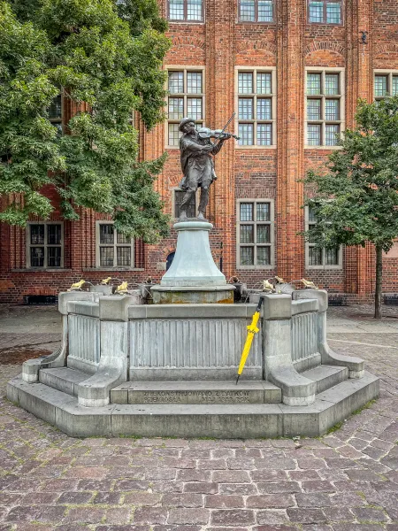 Brązowy posąg skrzypka na fontannie na historycznym placu w Gdańsku.