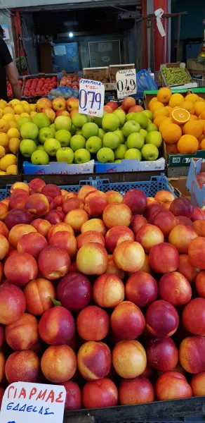 Un colorido puesto de frutas en un mercado griego, repleto de manzanas, naranjas y melocotones frescos.