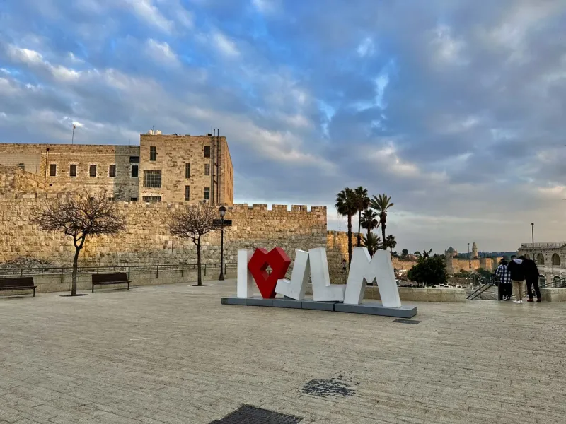 Turistas visitan el icónico letrero "I ♥ JLM" en Jerusalén, con las murallas de la Ciudad Vieja al fondo.