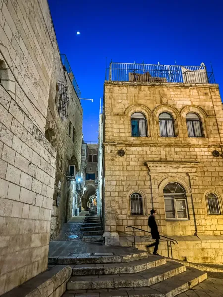 Una persona baja por una escalera de piedra en la iluminada Ciudad Vieja de Jerusalén por la noche.