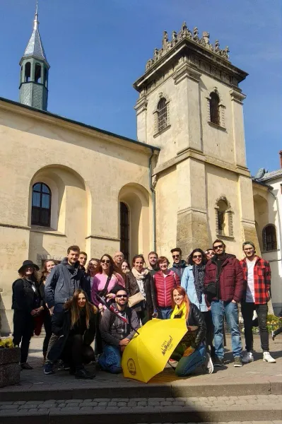 Szczęśliwi turyści na bezpłatnej wycieczce po Krakowie, w Polsce, pozują przed zabytkowym budynkiem.