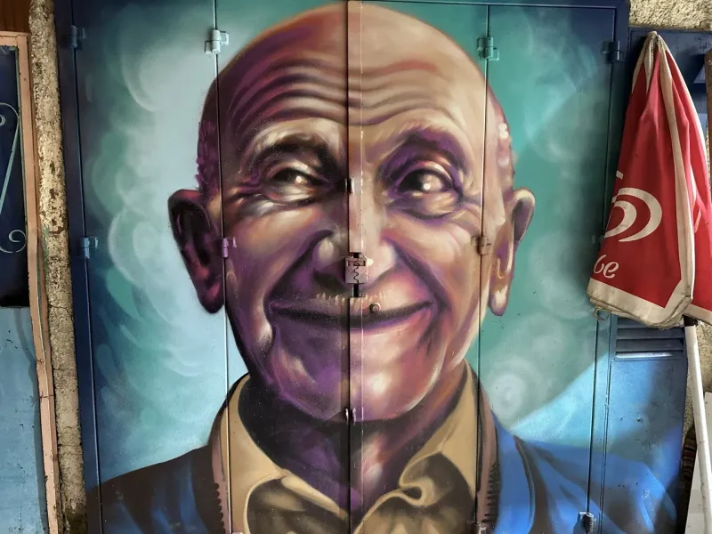 Lebhaftes Street-Art-Wandgemälde eines lächelnden älteren Mannes in Lissabon, Portugal.