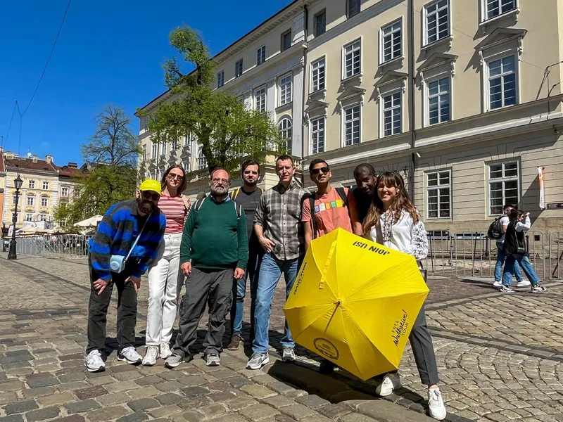 Eine vielfältige Gruppe von sieben Personen auf einer Kopfsteinpflasterstraße in Lwiw, mit einem Reiseleiter und einem gel...