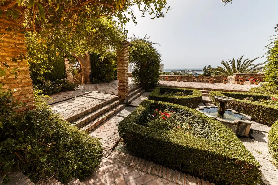 Sereno jardín en Málaga, España, con una fuente y vistas a la costa.