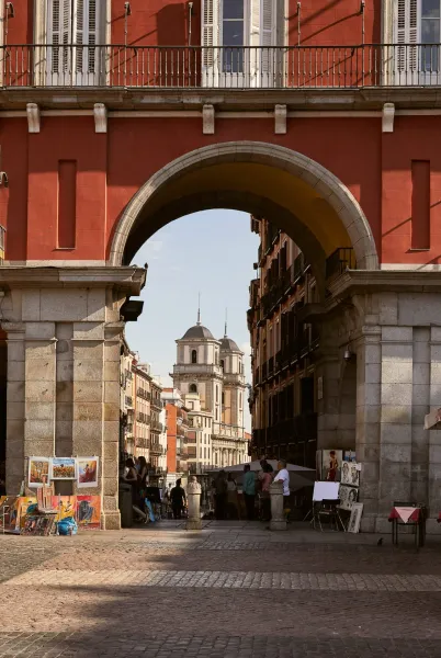 A picturesque archway in Madrid reveals a charming street scene with artists and historic buildings.