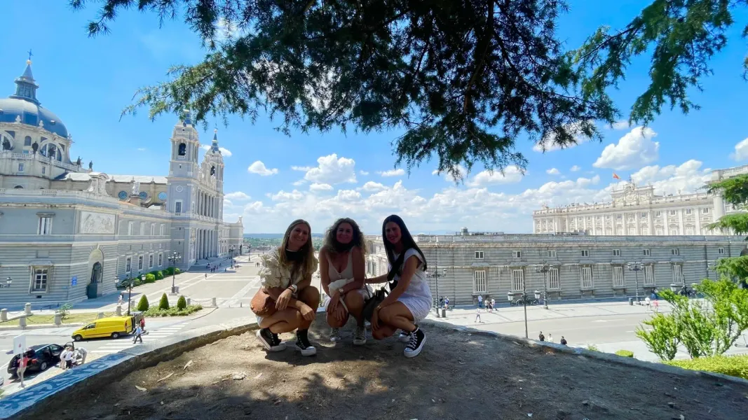 Drei Freundinnen genießen einen Städtetrip in Madrid, mit der Almudena-Kathedrale und dem Königspalast im Hintergrund.