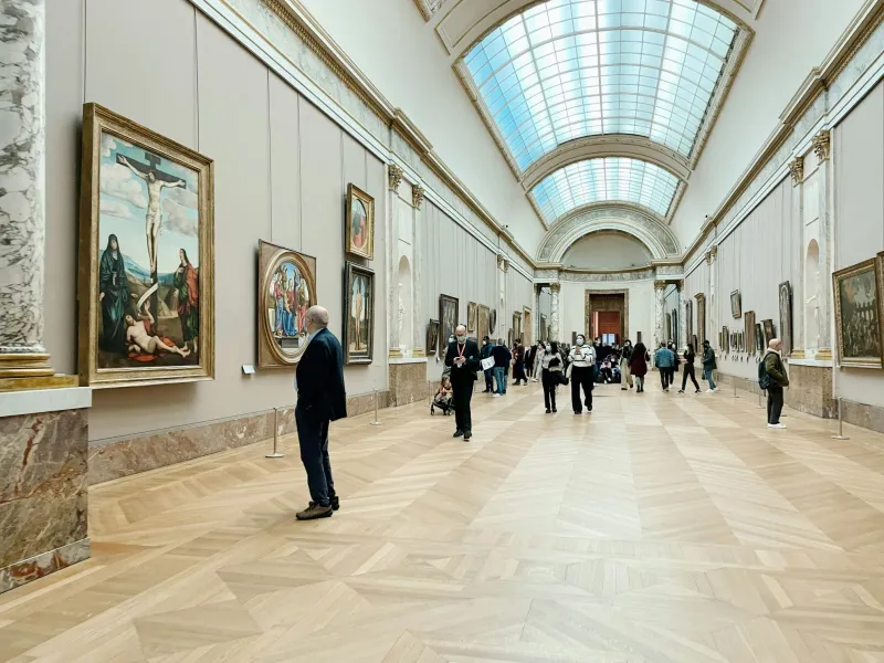 Tourists exploring a grand museum hall filled with art.