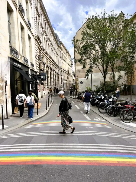 Ein Fußgänger überquert einen Regenbogen-Zebrastreifen in einer charmanten Pariser Straße.