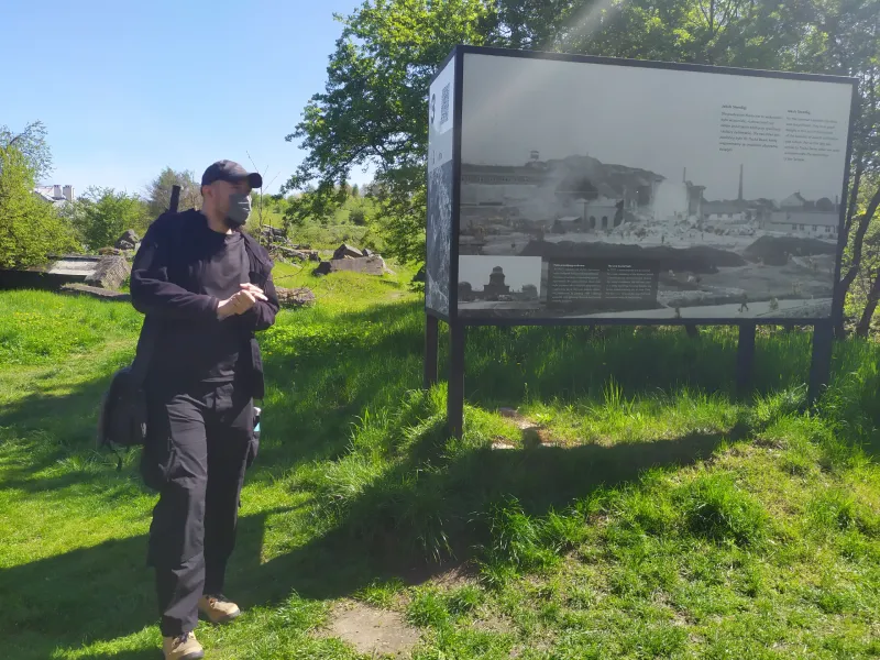 Ein Tourist erkundet eine historische Stätte in Polen und liest eine Informationstafel mit historischen Fotos.