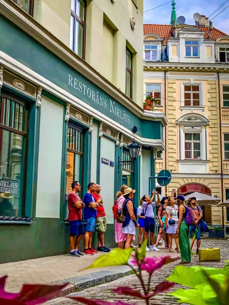 Un grupo de turistas explora las encantadoras calles de Riga, Letonia, haciendo una pausa frente a un restaurante histórico.