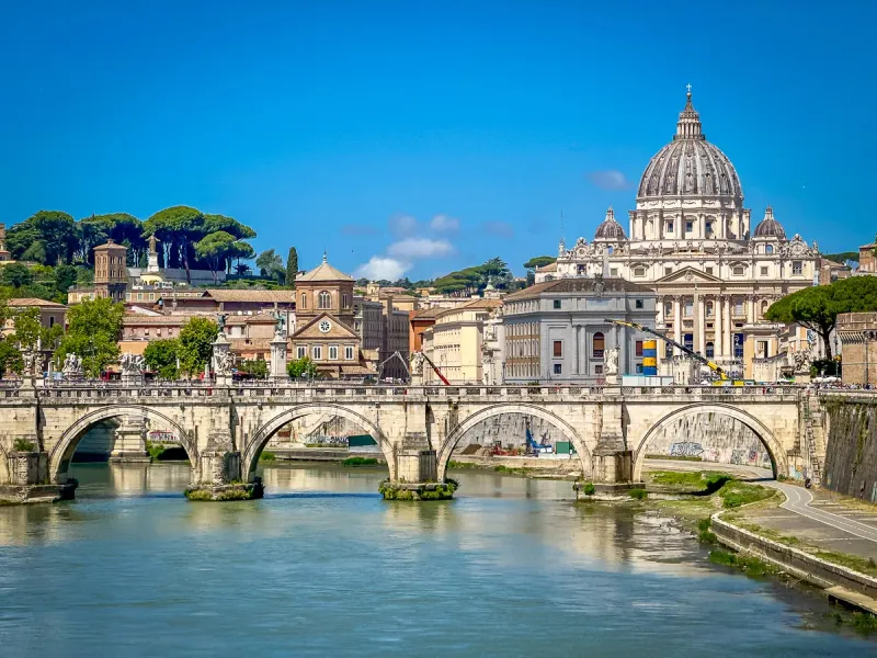 Most Anioła nad Tybrem, z kopułą Bazyliki Świętego Piotra i rzymskimi budynkami pod błękitnym niebem.
