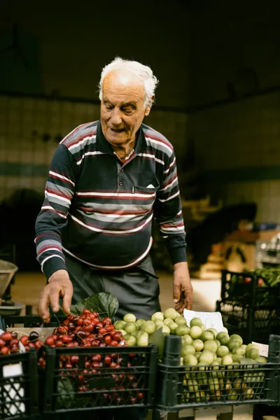 An elderly vendor smiles while arranging cherries and plums at a Roman market.