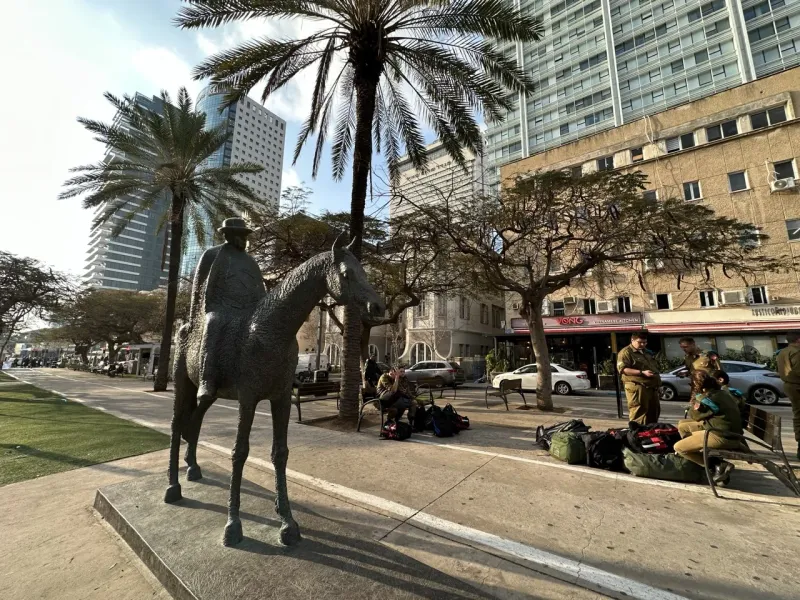 Bronzestatue eines Mannes zu Pferd in Tel Aviv, umgeben von Palmen und modernen Gebäuden.
