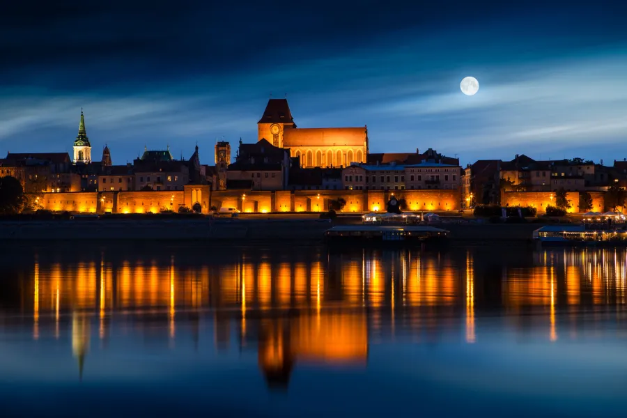 Nocny widok Starego Miasta w Toruniu, odbijający się w Wiśle.