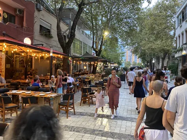 Tętniąca życiem ulica miejska w nocy z restauracjami na świeżym powietrzu i pieszymi.