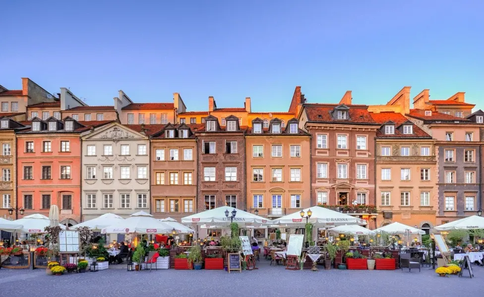 Warsaw's Old Town Square at sunset, featuring colorful buildings and a charming outdoor cafe.