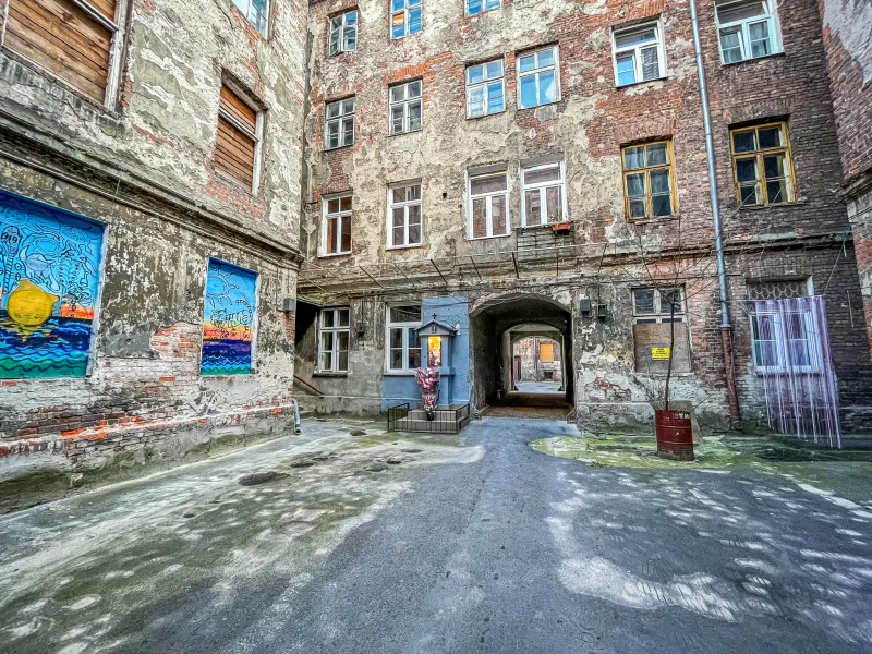 Explore un patio oculto de Varsovia con edificios antiguos de ladrillo, arte callejero y un pequeño santuario.