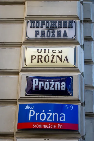 Cztery znaki uliczne na budynku w Warszawie, wszystkie wskazujące ulicę Próżną.