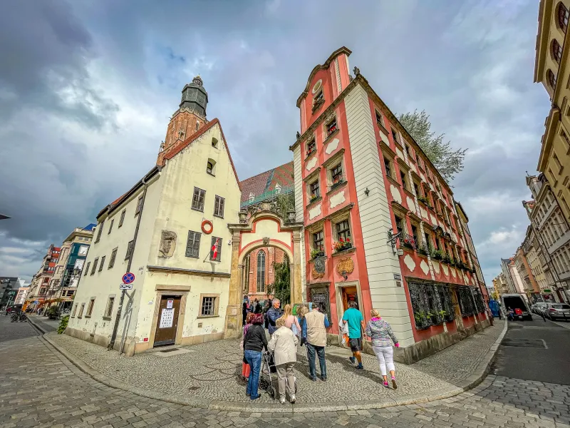 Grupa turystów zwiedza historyczne ulice Wrocławia, mijając piękne budynki.