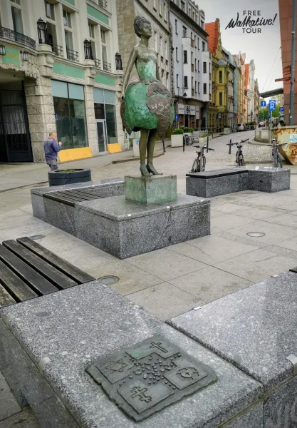 Brązowa statua kobiety trzymającej globus w centrum Wrocławia.
