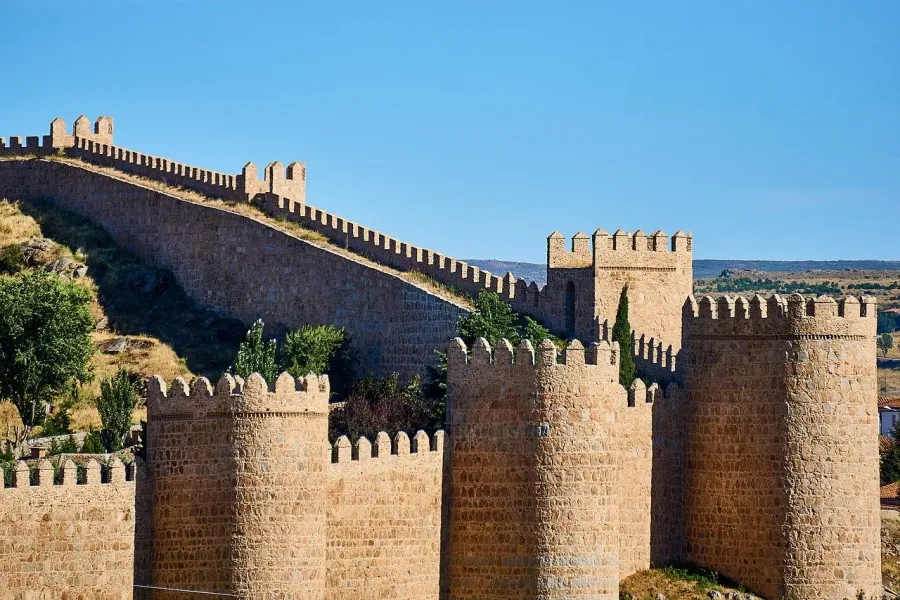 Las murallas medievales de piedra de Ávila, con sus almenas y torres, en un día soleado con un cielo azul y despejado.