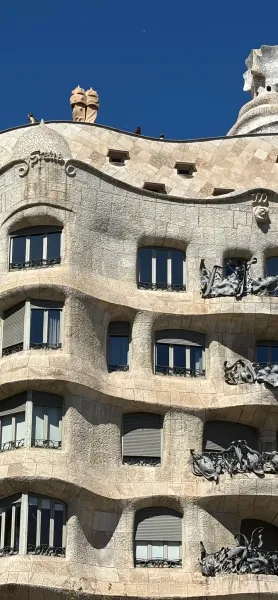 Detalle de la fachada ondulada de piedra de la Casa Milà con ventanas oscuras, persianas grises y balcones de hierro forjado.