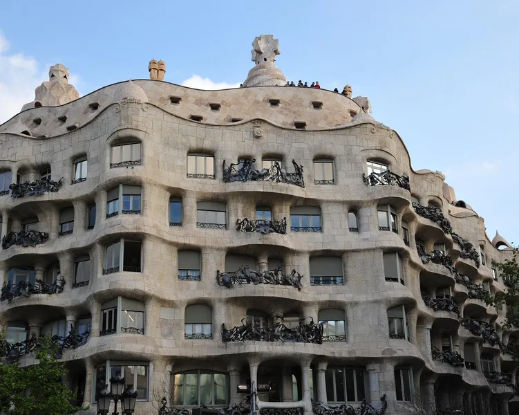 Fachada de piedra curvada de Casa Milà (La Pedrera) con balcones de hierro ornamentados bajo cielo azul, diseñada por Gaudí.