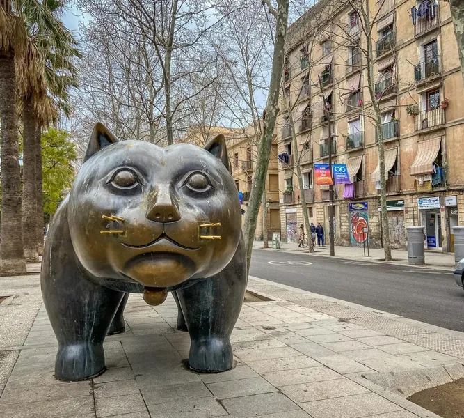 Large bronze cat sculpture by Botero on a sidewalk in Barcelona, with buildings and palm trees in the background.