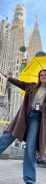 A smiling Walkative guide with a yellow umbrella in front of the Sagrada Familia in Barcelona, with its towers under construc