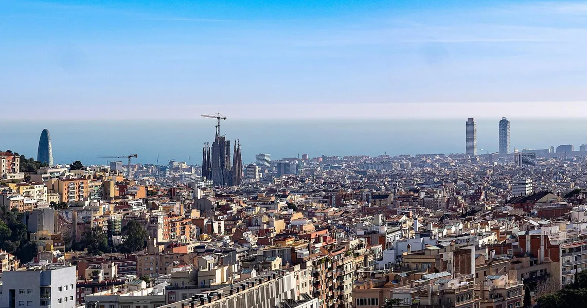 Panoramablick auf Barcelona mit der Sagrada Familia im Bau, dem Agbar Tower und zwei Wolkenkratzern am Meer.